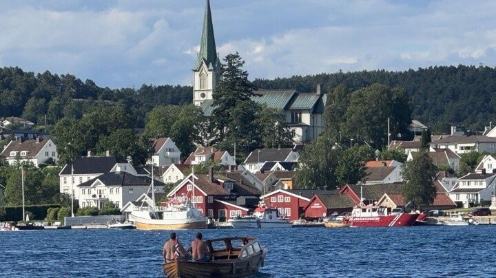 Båt på fjorden foran tettsted med kirke og brygger