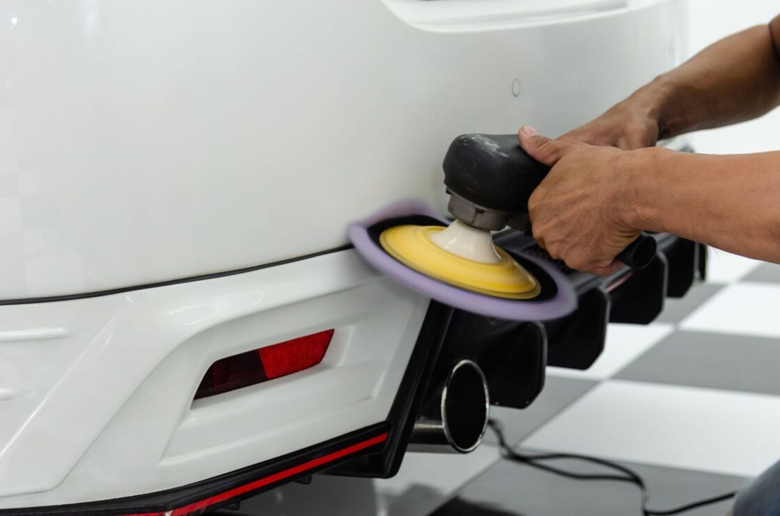 En person polerer et hvitt båtskrog med en elektrisk poleringsmaskin