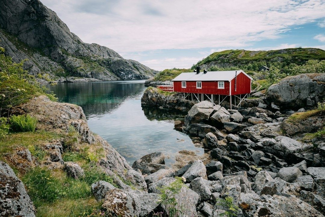 Rød sjøbu på påler ved et smalt, steinete kystfarvann